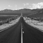 Black and white view of a long, empty highway stretching into distant desert mountains.