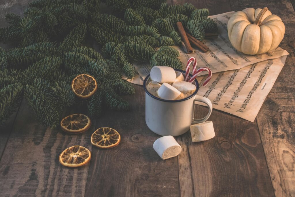 Cozy autumn flat lay with hot chocolate, marshmallows, candy canes, evergreen branches, and dried oranges.