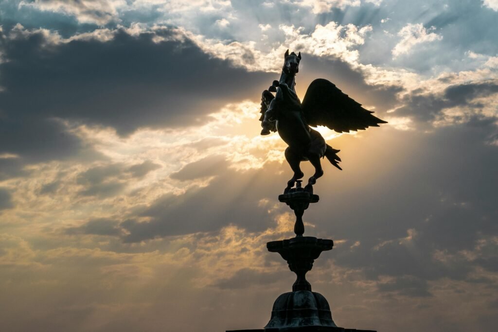 A stunning silhouette of a Pegasus sculpture against a dramatic sunset sky with sun rays.