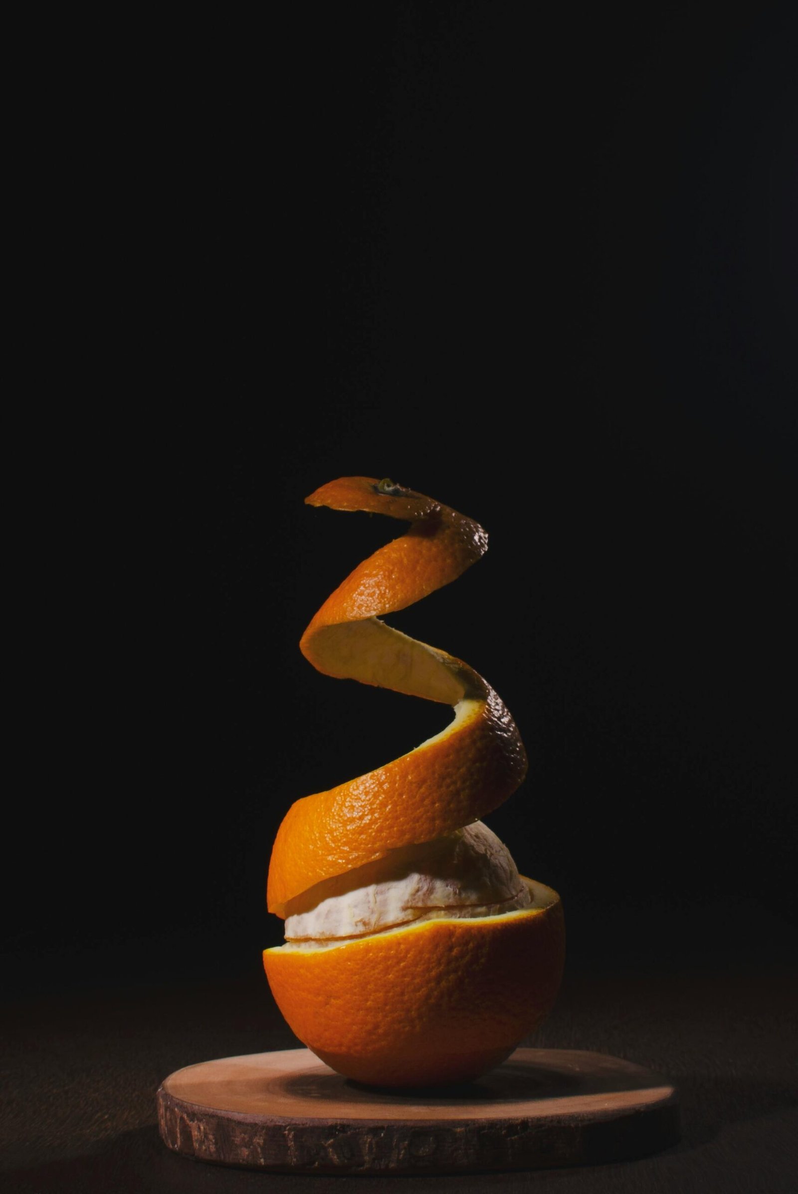 A creatively peeled orange with spiral skin on a wooden board against a dark background.