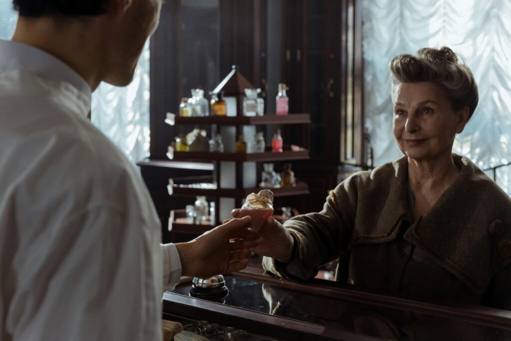 A senior woman receives a perfume bottle from a pharmacist inside a vintage pharmacy.