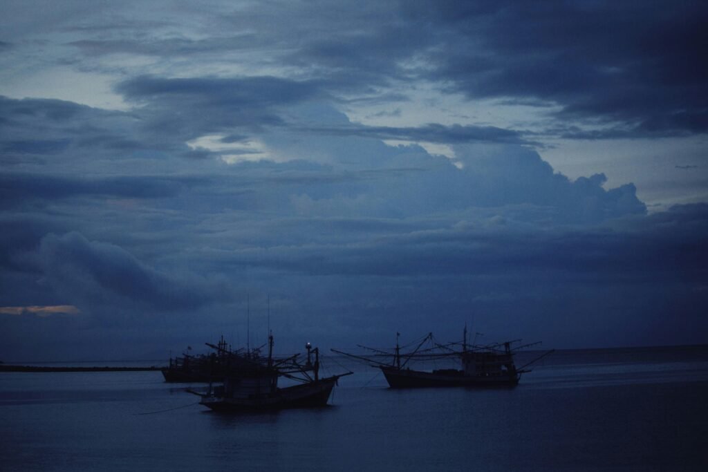 Tranquil scene of fishing boats on the sea under a dramatic, overcast evening sky.