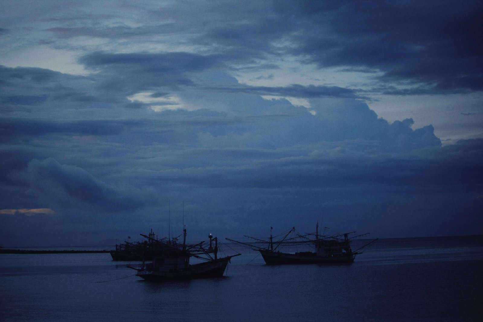 Tranquil scene of fishing boats on the sea under a dramatic, overcast evening sky.