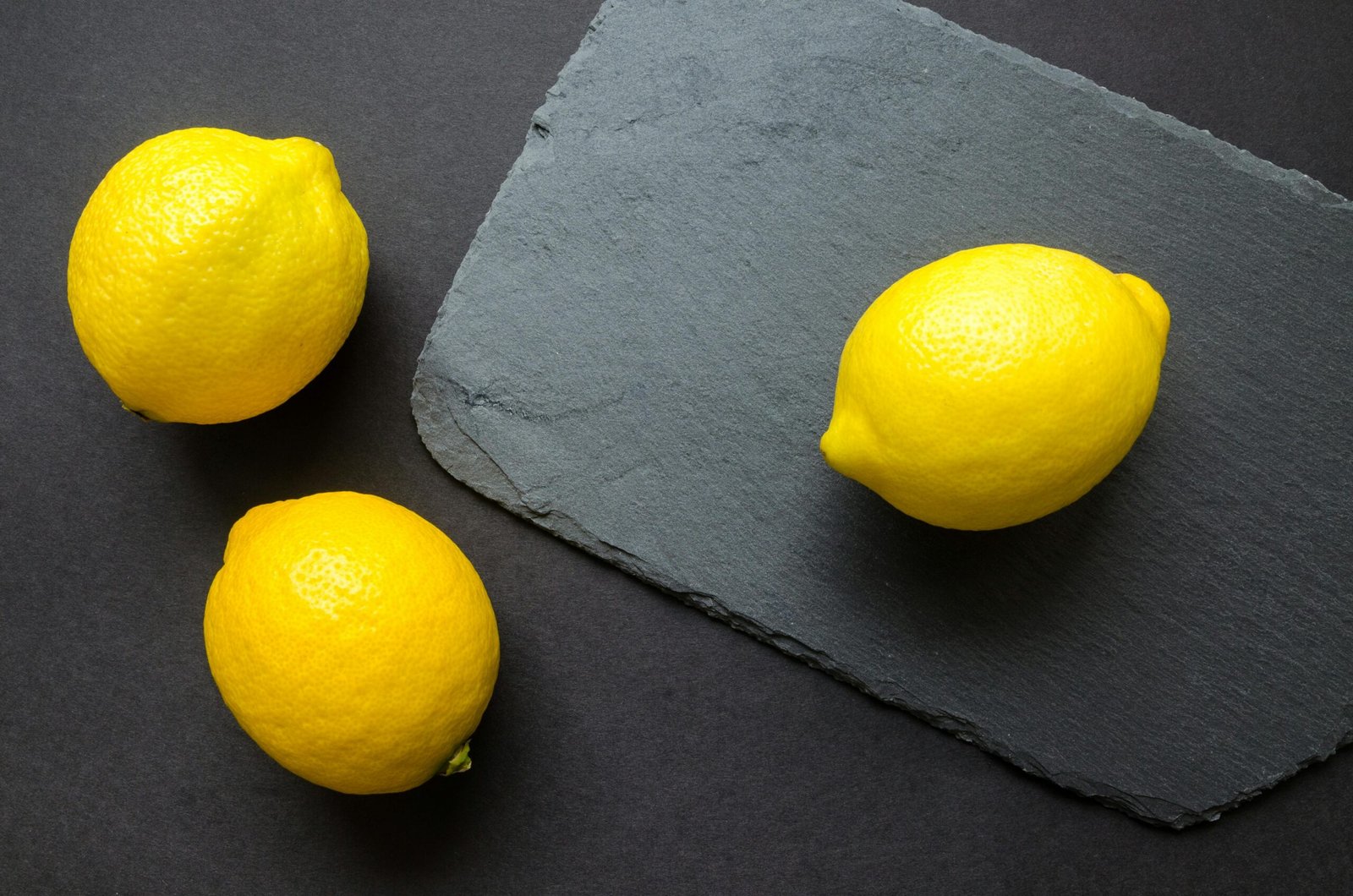 High-angle shot of vibrant lemons on dark slate, emphasizing freshness.