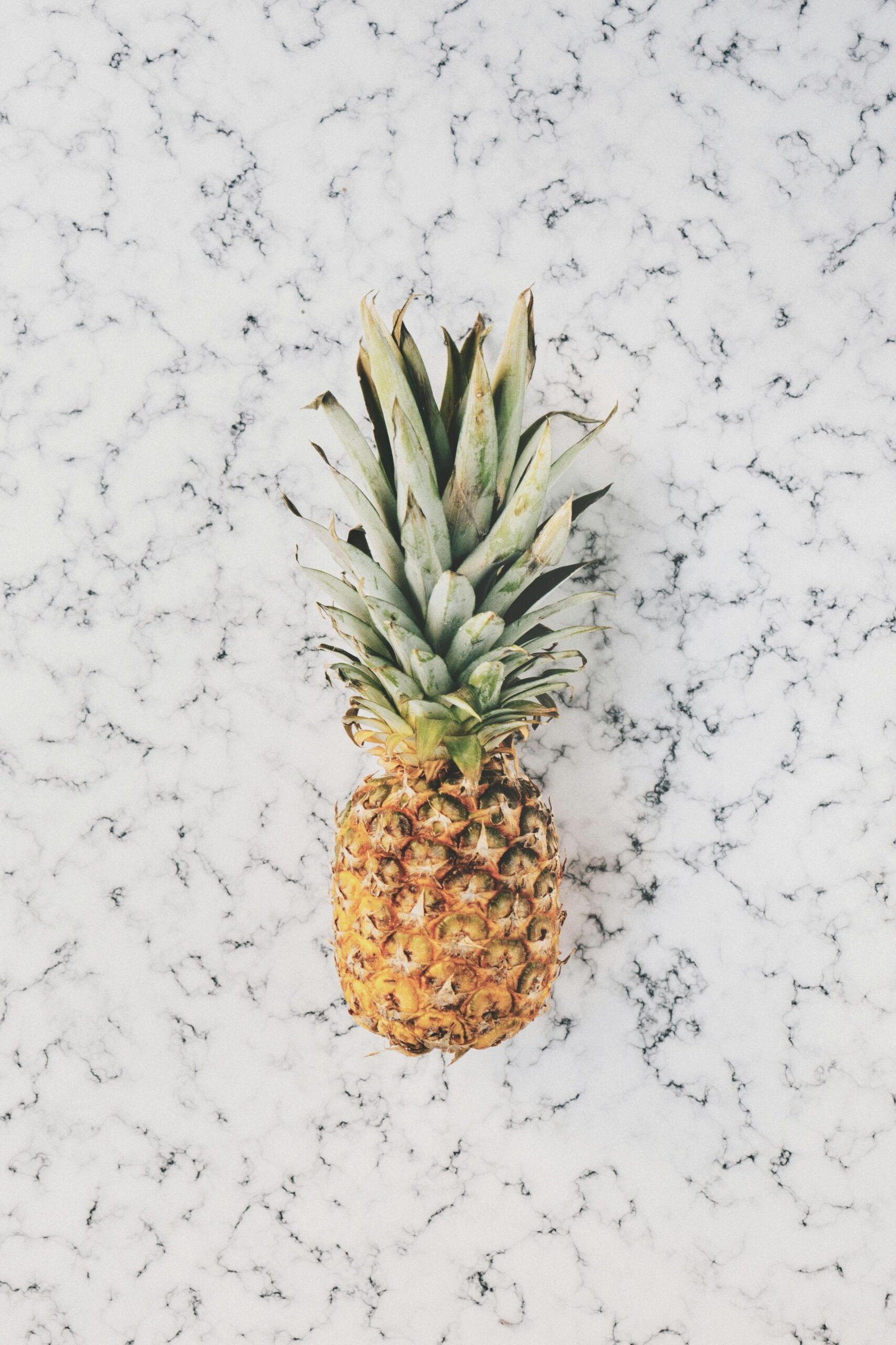 A vibrant pineapple on a minimalist marble texture surface, evoking tropical freshness and health.
