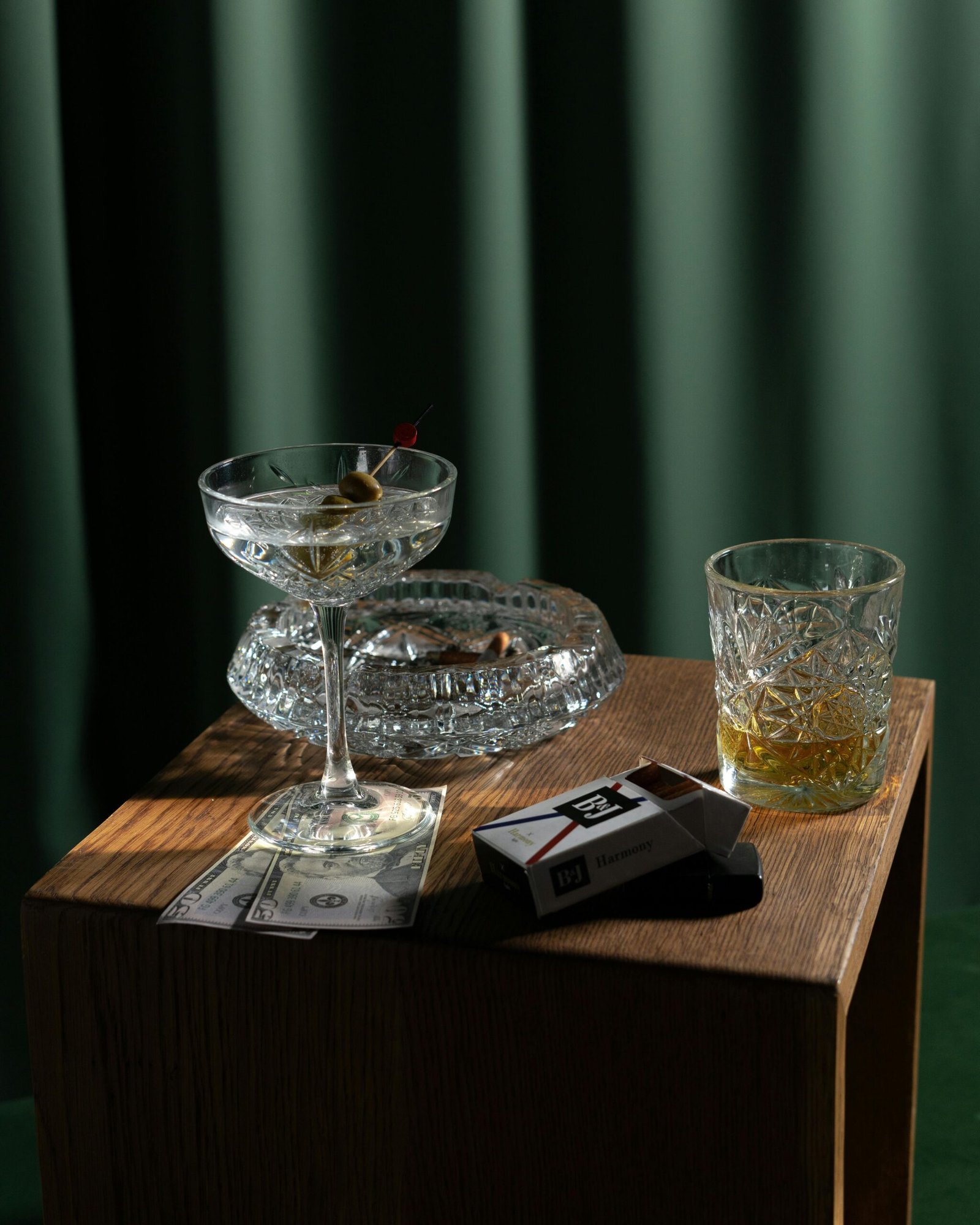A classic cocktail and whiskey glass on a wooden table with cash and cigarettes.