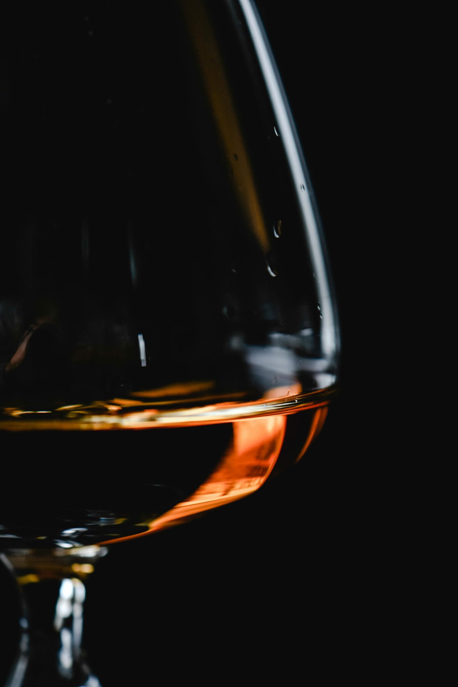 Elegant close-up of cognac glass with amber liquid illuminated softly against a dark background.